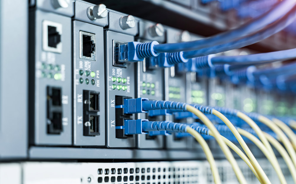 A detailed close-up of professional telecommunications equipment with several blue UTP network cables and yellow fiber optic cables connected to network ports.