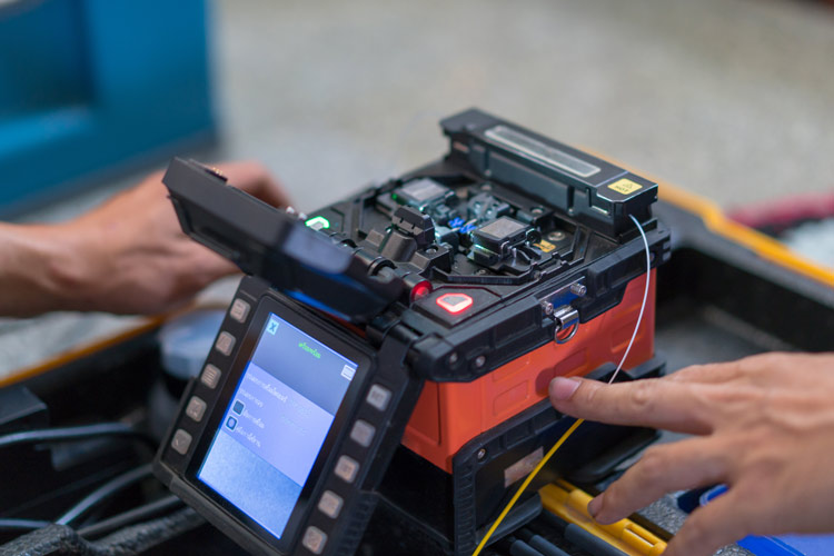 A technician works with a professional fiber optic fusion splicer used to splice fiber optic cables.