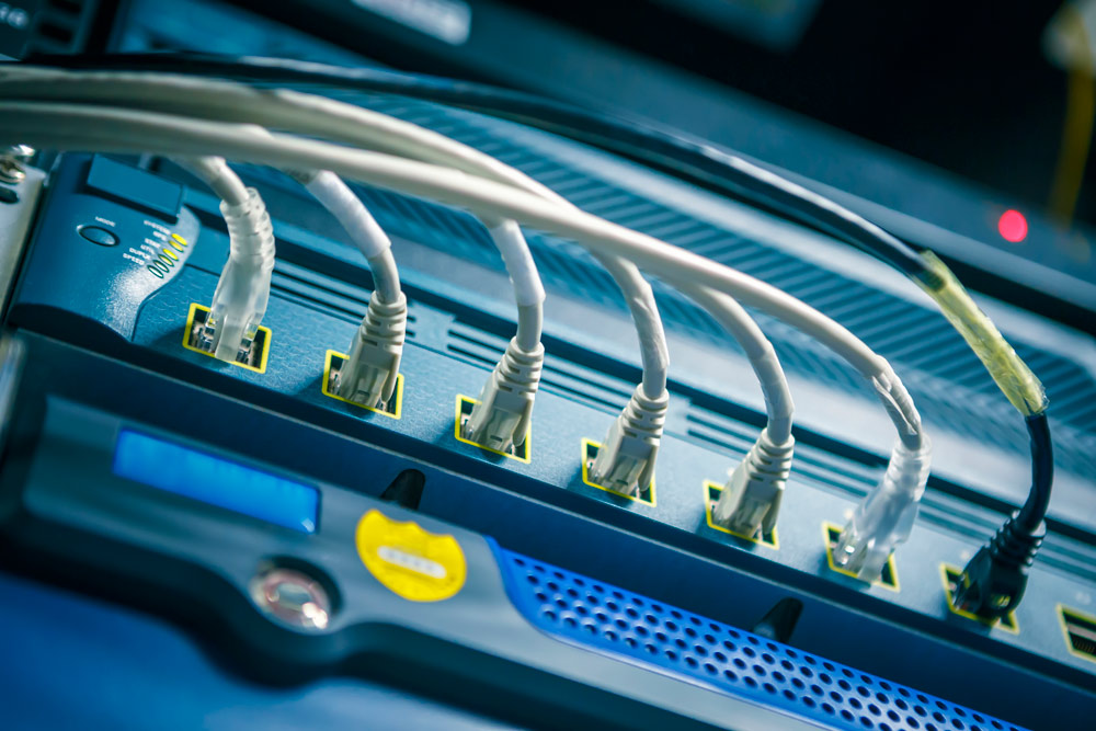 The image shows a professional blue metal network hub with several white network cables connected in a row of ports.